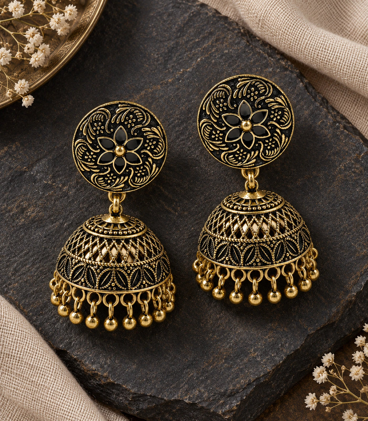 JIMIKI Antique Gold Black Floral Disc Jhumka Earrings - pair styled on dark stone with linen #color_antique-gold-black