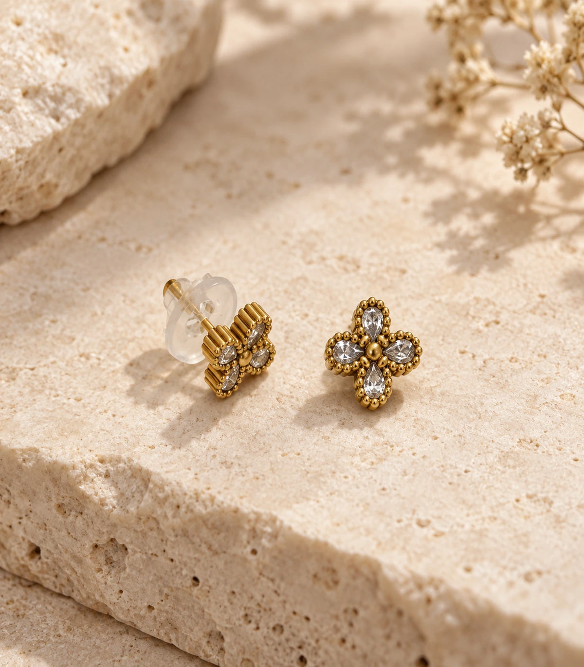 JIMIKI Antique Gold Crystal Clover Stud Earrings, matching pair arranged on a pale textured stone surface #color_antique gold