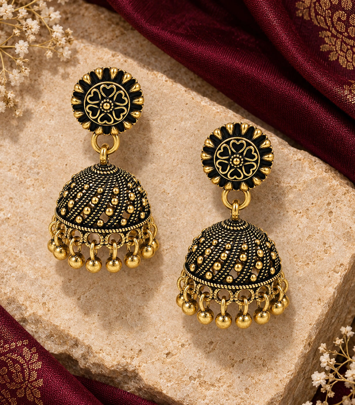 JIMIKI Antique Gold Floral Rosette Jhumka Earrings - Matching pair on pale stone beside maroon fabric #color_antique-gold