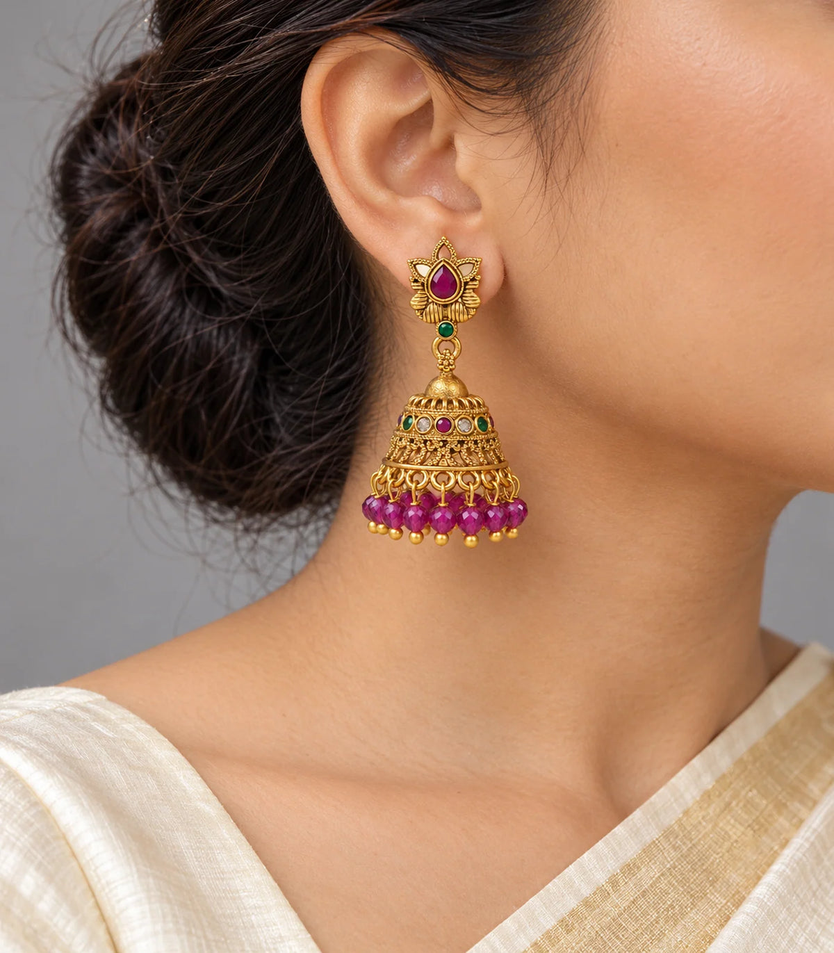 Antique gold-tone magenta lotus jhumka earrings worn with a cream outfit