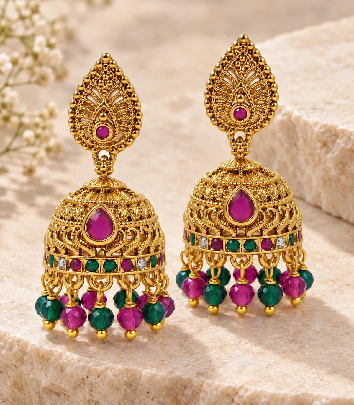 Matching pair of antique gold-tone magenta and green beaded jhumka earrings on a pale stone setting