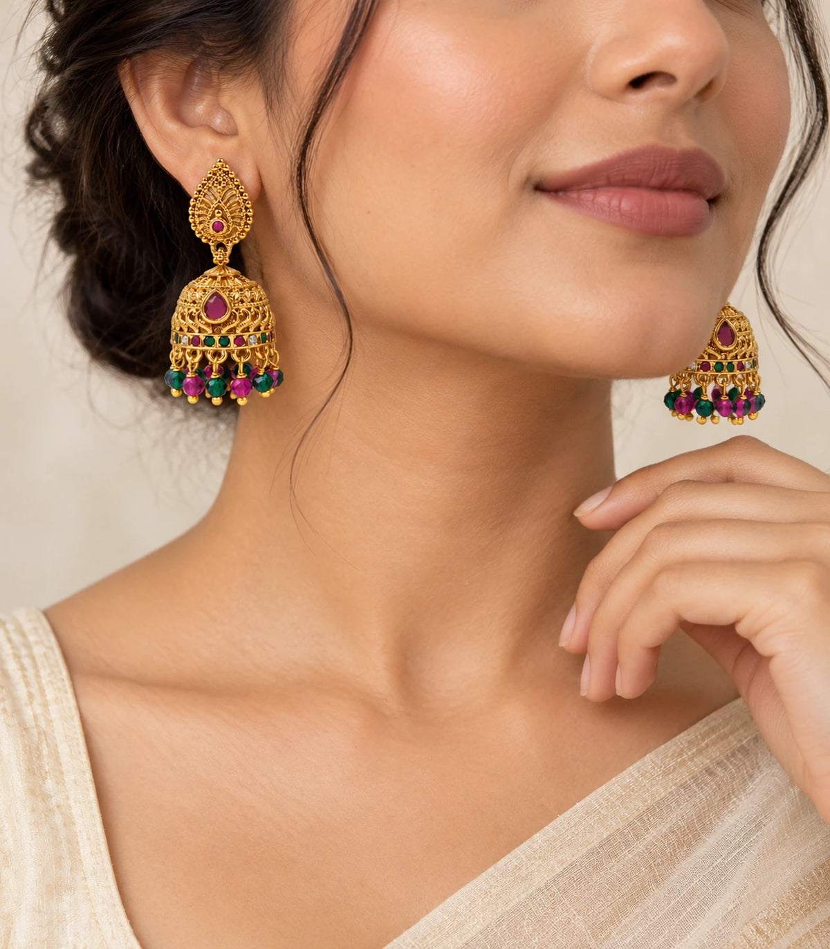 Antique gold-tone magenta and green beaded jhumka earrings worn with a cream sari