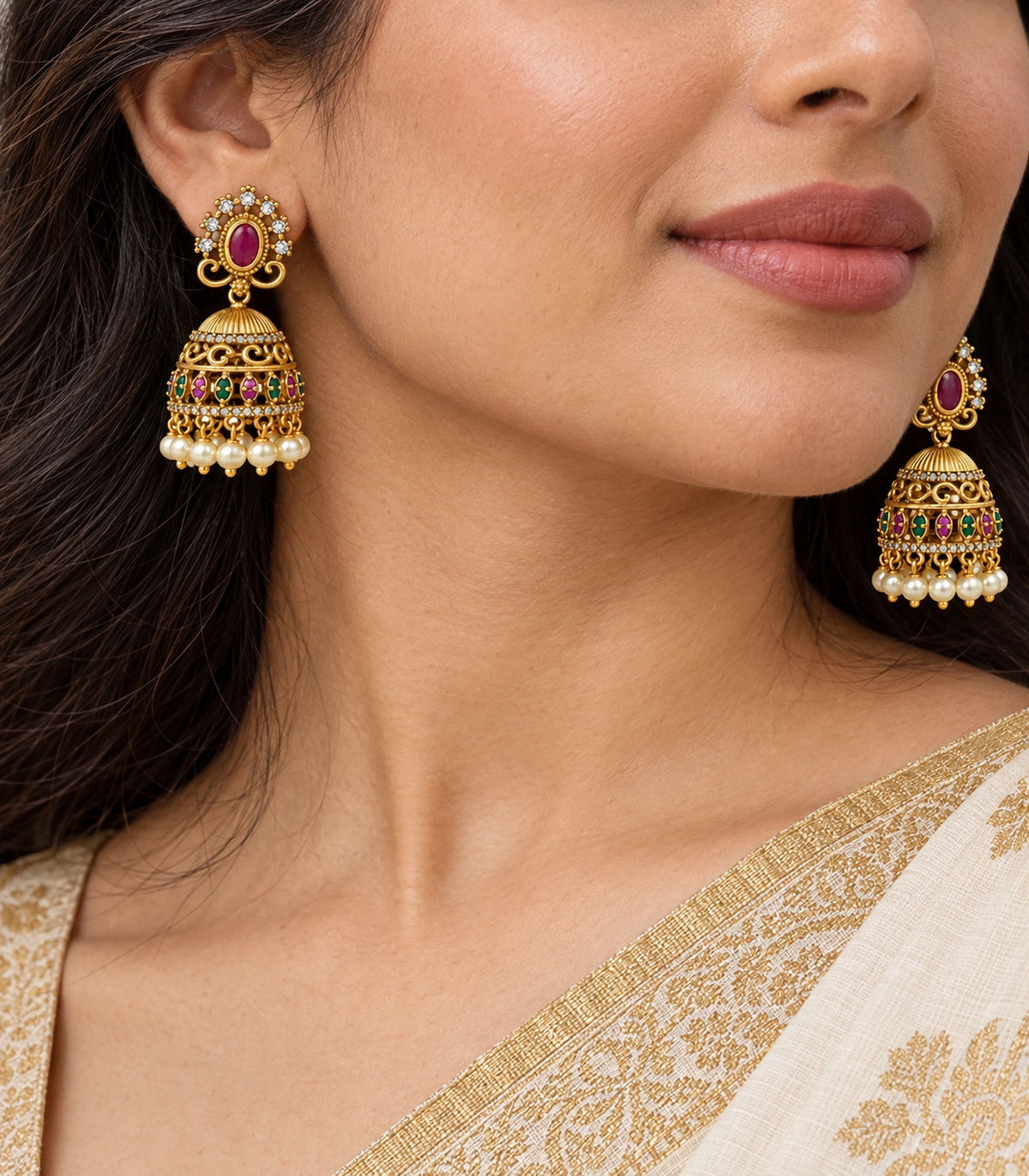 Close view of magenta stud, gold-tone scroll bell and pearl fringe on worn jhumka earrings