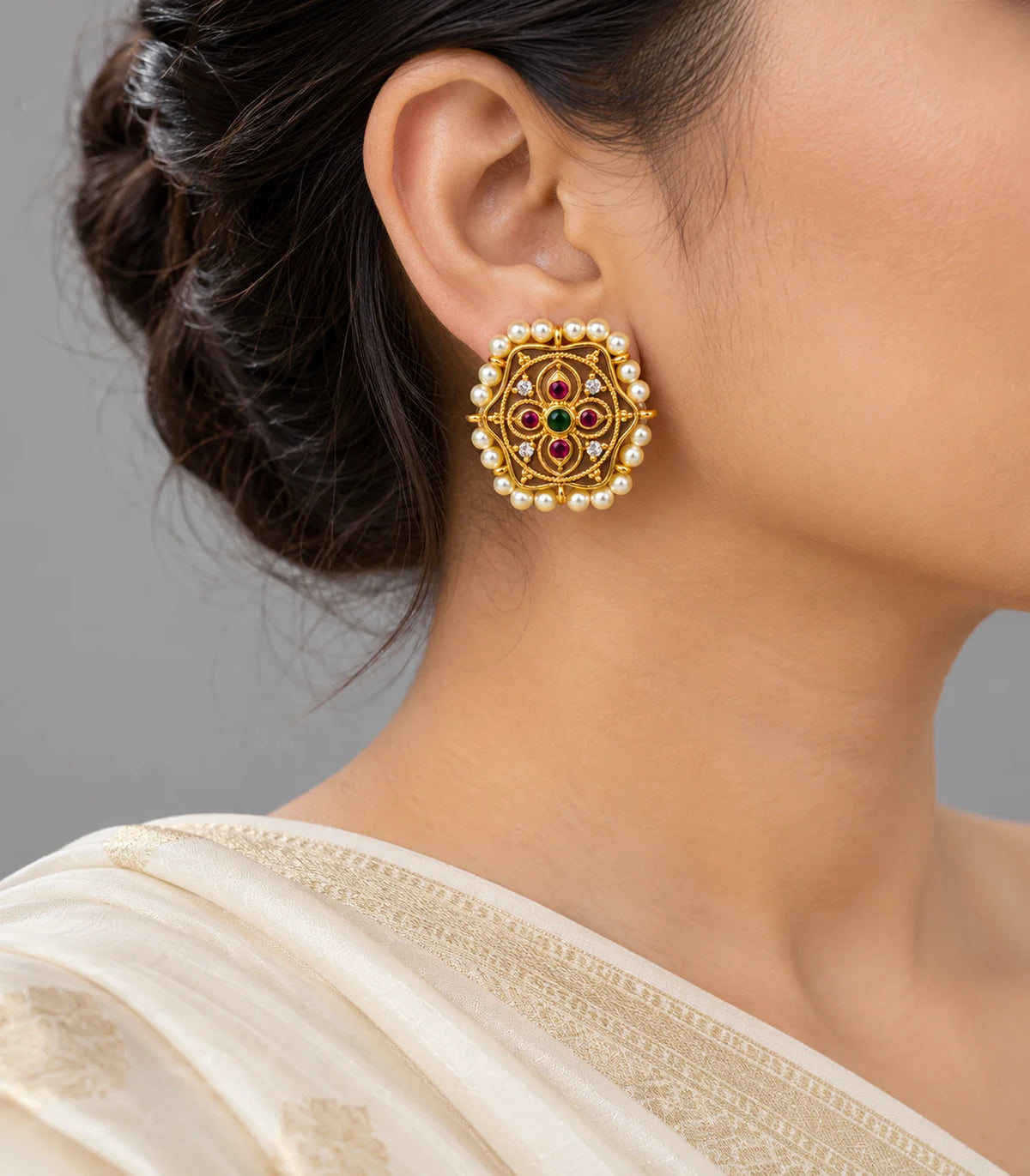 Antique gold-tone pearl-border studs worn with a cream outfit; magenta stones and green centres