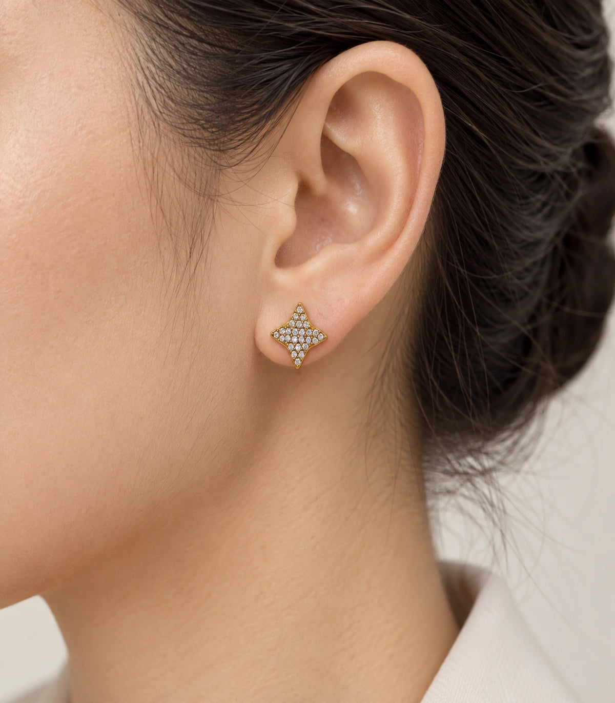 JIMIKI antique gold-tone four-point star stud earrings, alternate worn view showing the star stud on the earlobe #color_antique-gold