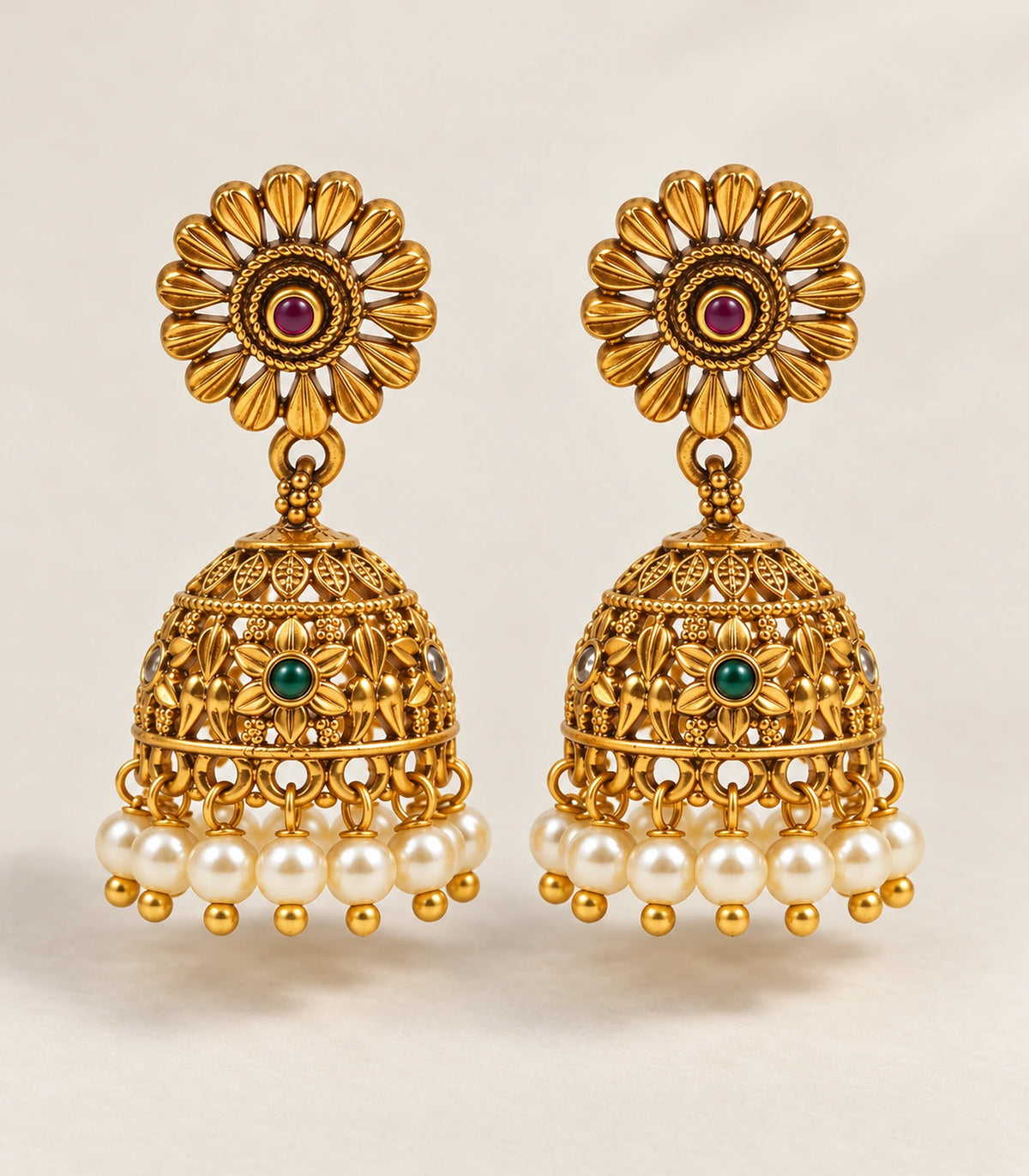 Complete pair of antique gold tone sunflower green and magenta pearl jhumka earrings on a neutral surface