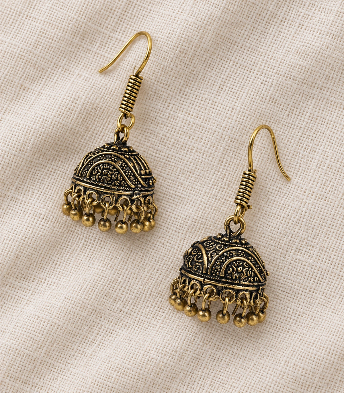 Antique gold-tone wave scroll jhumka pair arranged on textured ivory fabric #color_antique-gold
