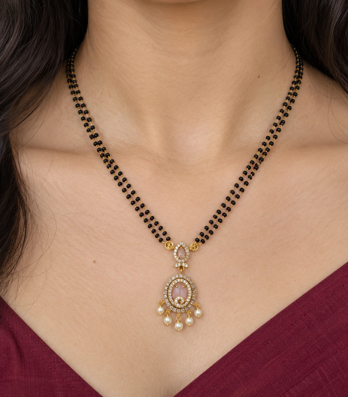 Close view of blush teardrop connector and oval scroll pendant with five pearl drops worn at the neckline