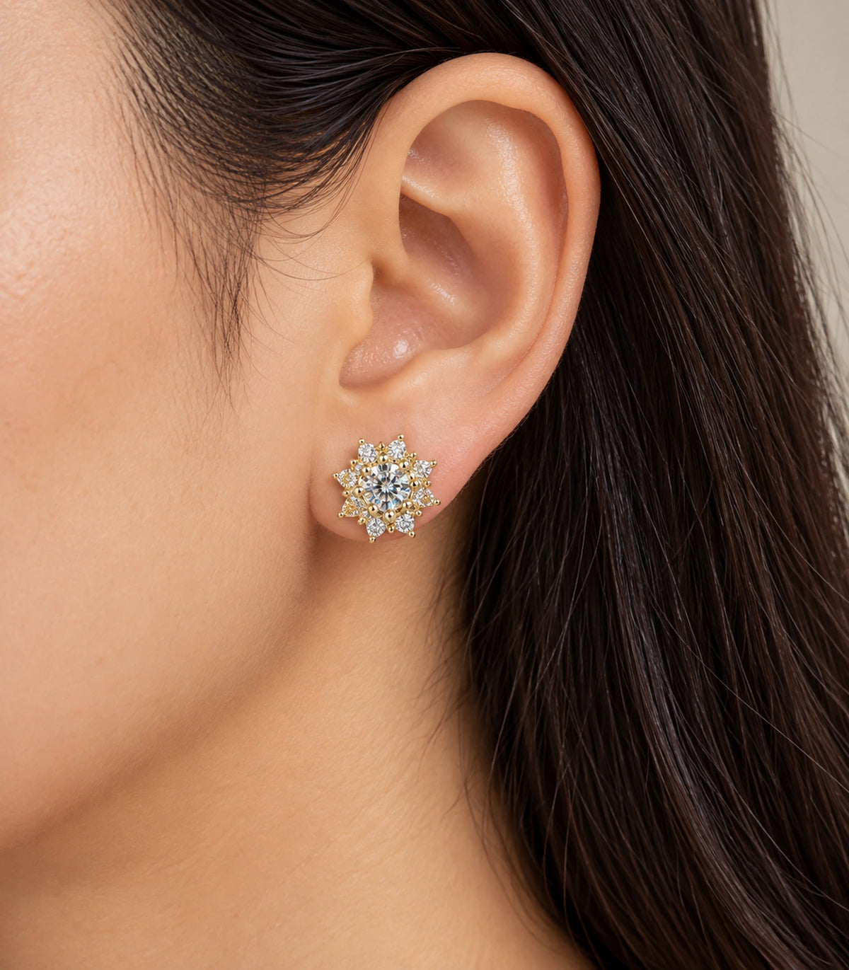 Gold-tone crystal sunburst stud earring worn on an ear