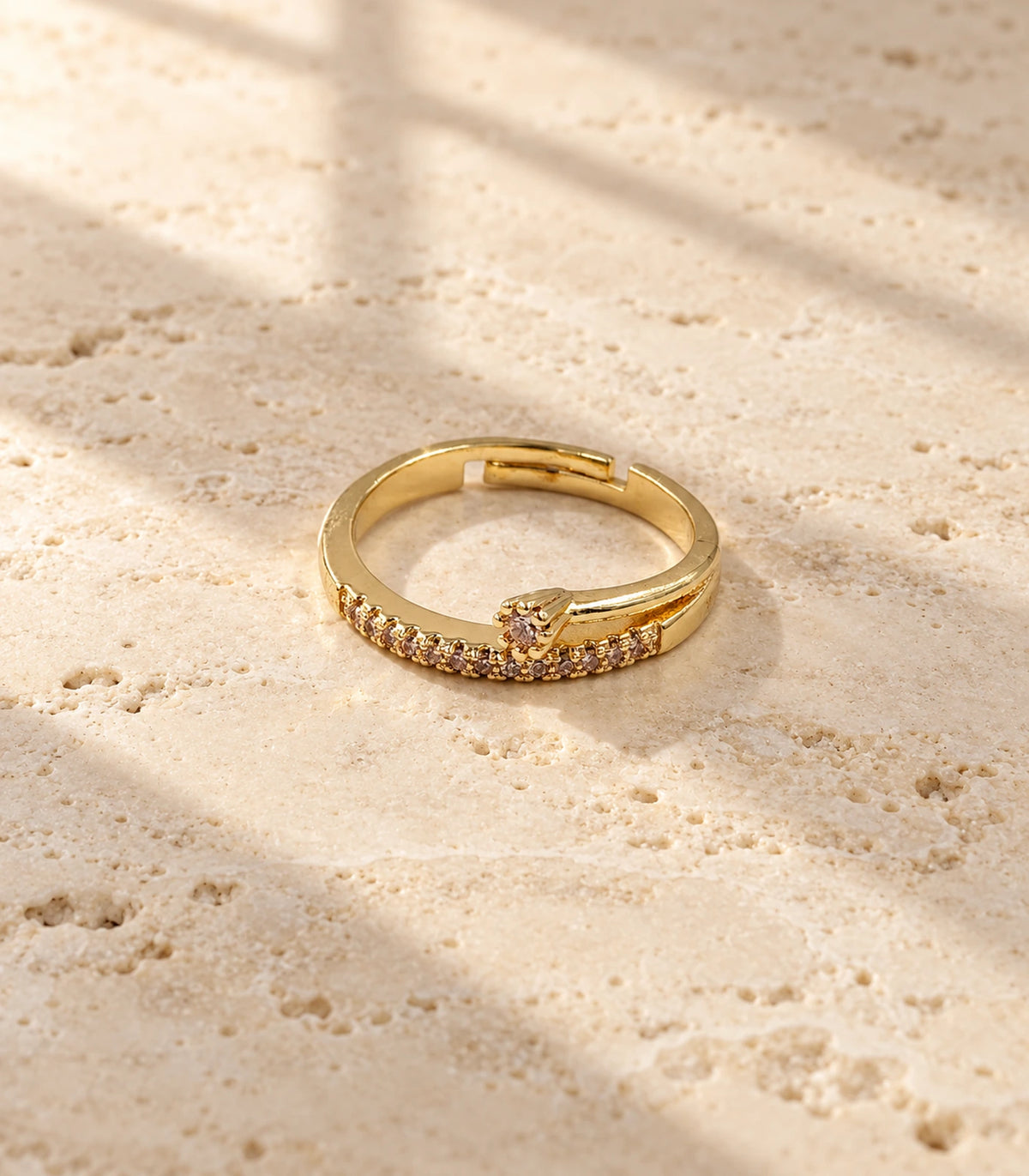 Complete gold-tone crystal wishbone arrow ring on a warm stone surface