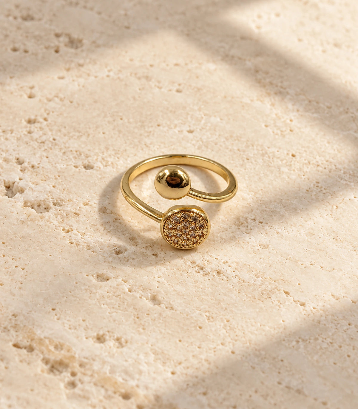 Gold Dual Disc Crystal Open Ring on a pale textured stone surface