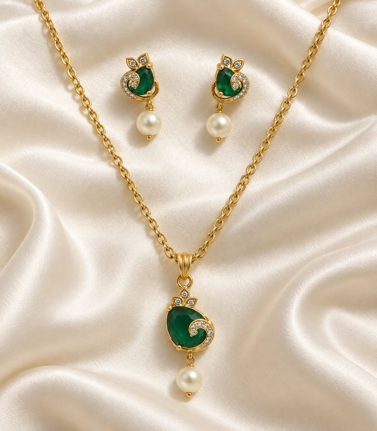 Gold-tone emerald-green crescent pendant necklace and matching earrings arranged on cream satin