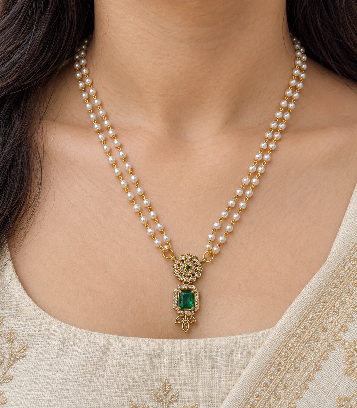 Closeup of the green pendant, circular clear-stone cluster and double pearl-style strands worn at the neckline