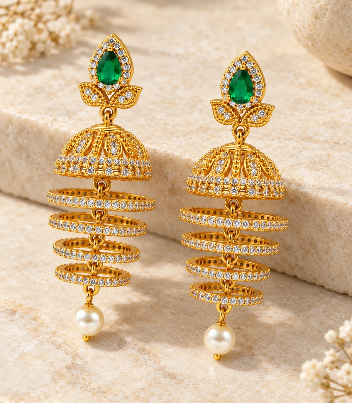 Complete matching pair of green and gold-tone hoop-drop earrings arranged on a cream stone surface