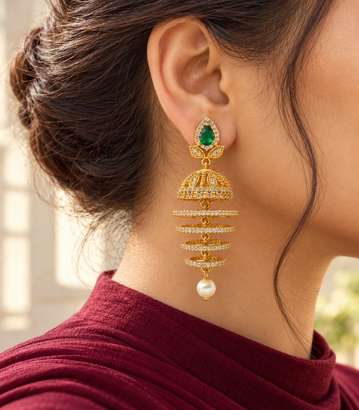 Editorial single-ear worn view with burgundy clothing, showing the complete green and gold-tone earring