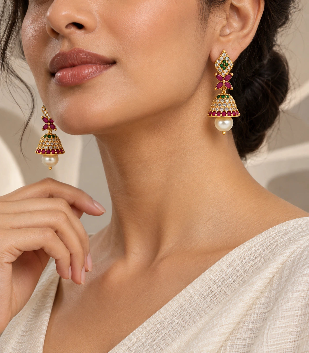 Turned worn view of gold-tone green and magenta jhumkas with pearl-style drops and ivory sari