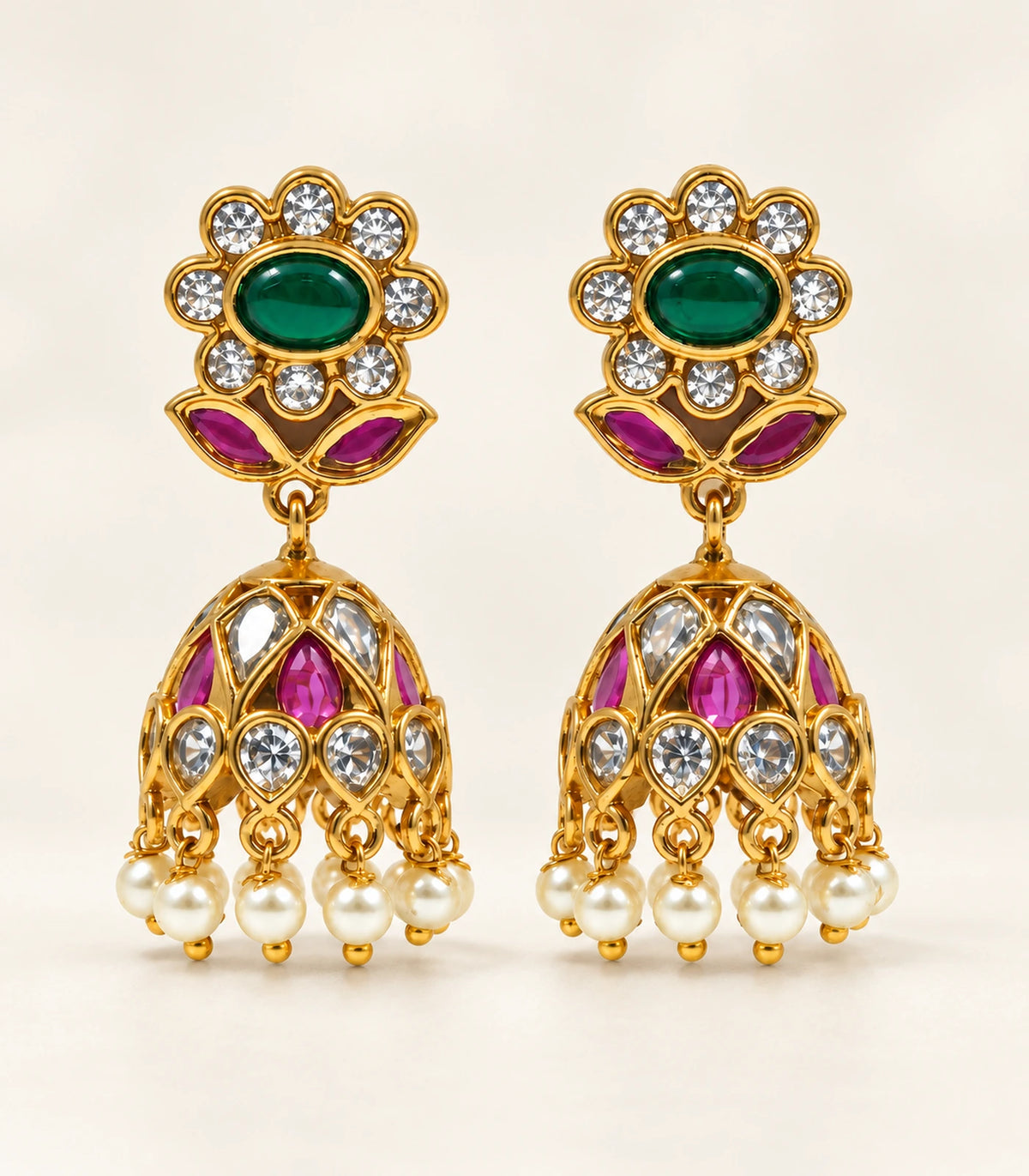 Complete matching pair of emerald-green and magenta floral pearl-fringe jhumka earrings on a cream surface