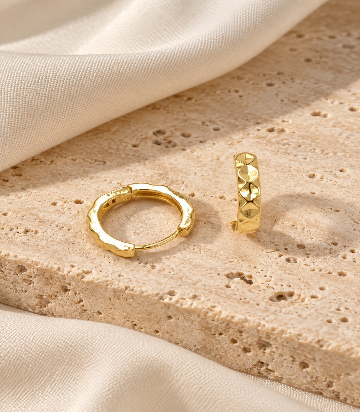 JIMIKI gold faceted diamond pattern huggie earrings, pair styled on textured stone #color_gold-tone