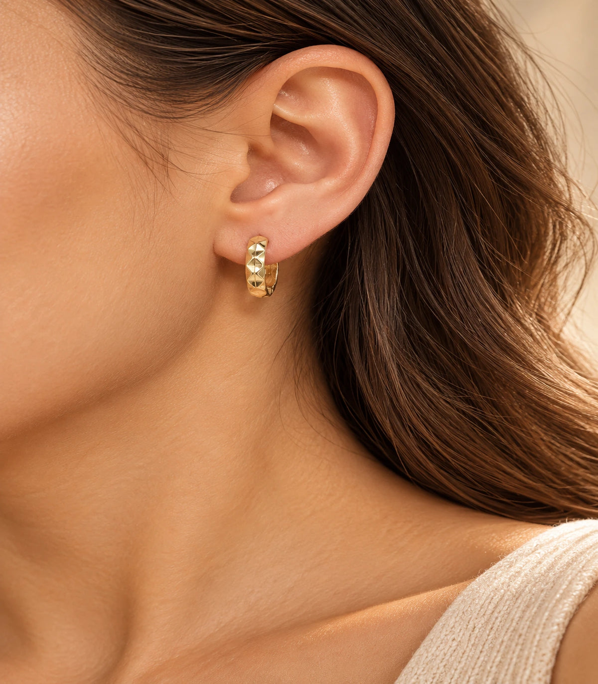 JIMIKI gold faceted diamond pattern huggie earrings, worn in warm editorial lighting #color_gold-tone
