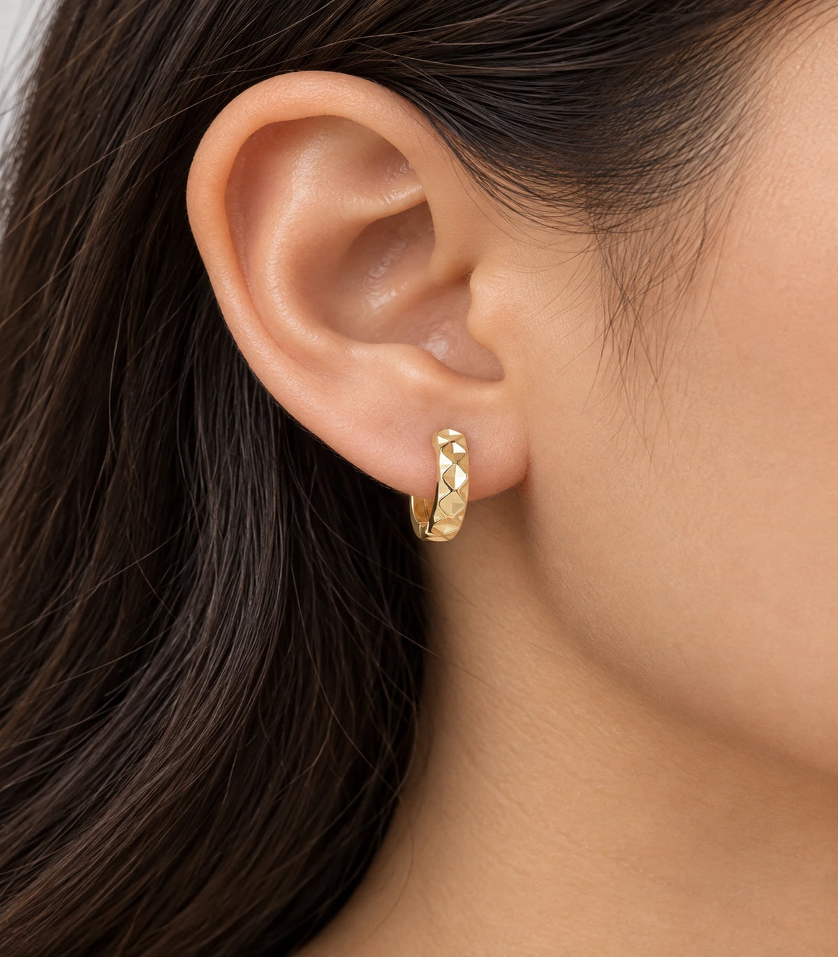 JIMIKI gold faceted diamond pattern huggie earrings, worn on the ear #color_gold-tone