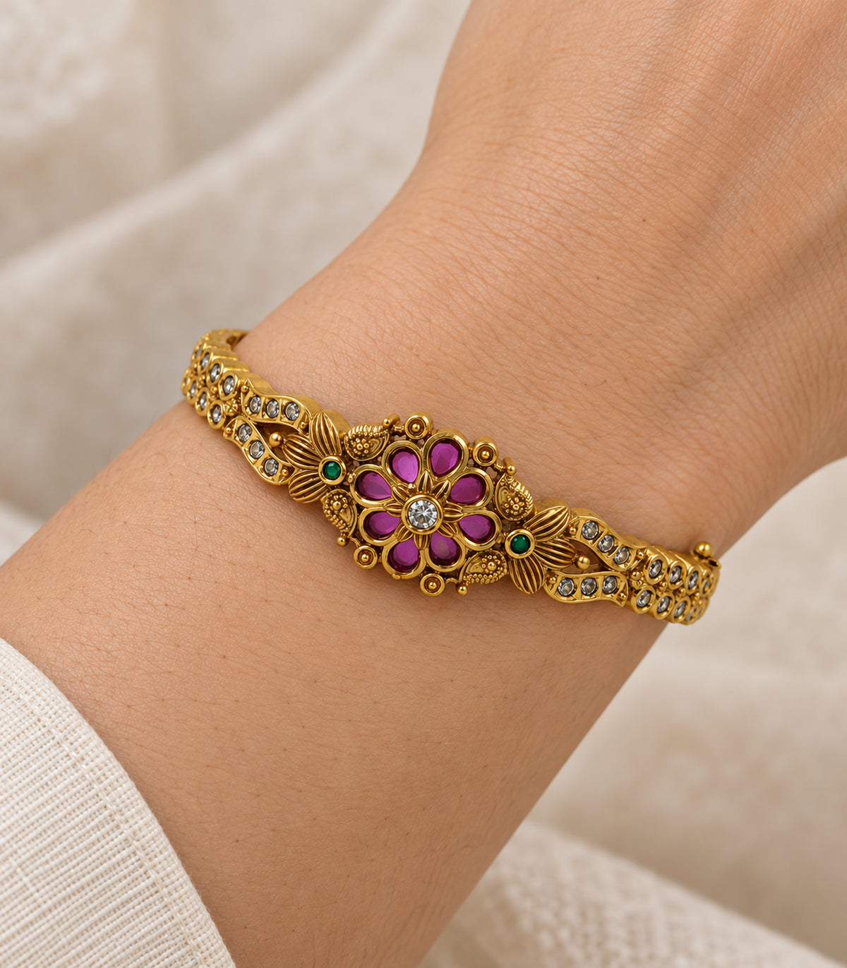 Close-up of the magenta floral centre and green side accents of the gold-tone bangle