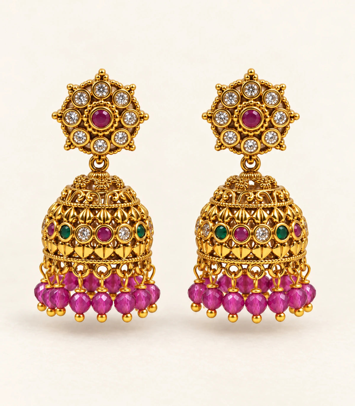 Complete pair of magenta and green gold-tone jhumka earrings in a styled flatlay