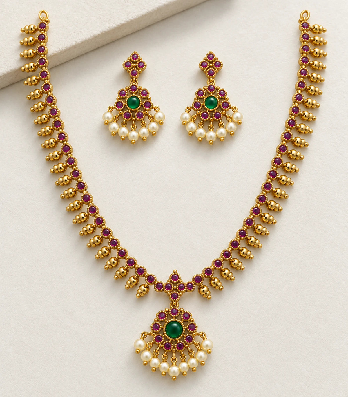 Detailed view of the magenta and green necklace set and matching earrings on fabric