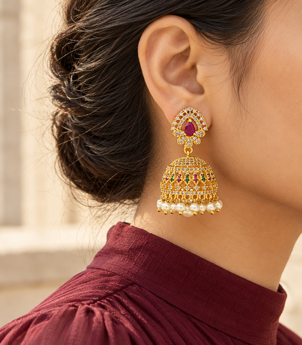 Gold-tone magenta and green lattice jhumka earring in a side view with burgundy clothing