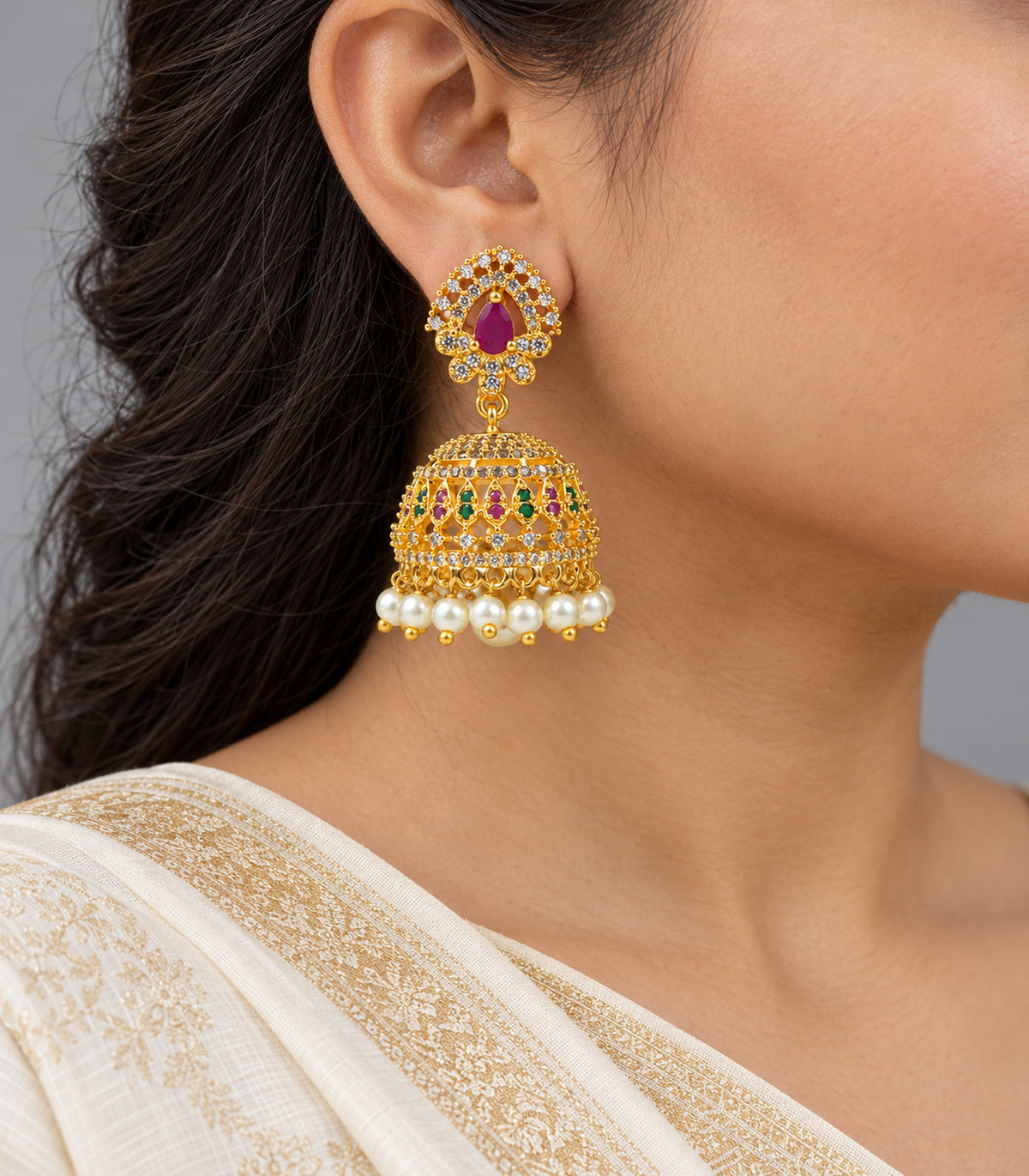 Gold-tone magenta and green lattice jhumka earring worn at one ear with ivory saree styling