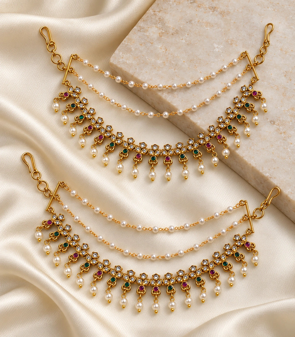 Gold tone magenta green triple-leaf pearl ear chain pair arranged on ivory silk and stone