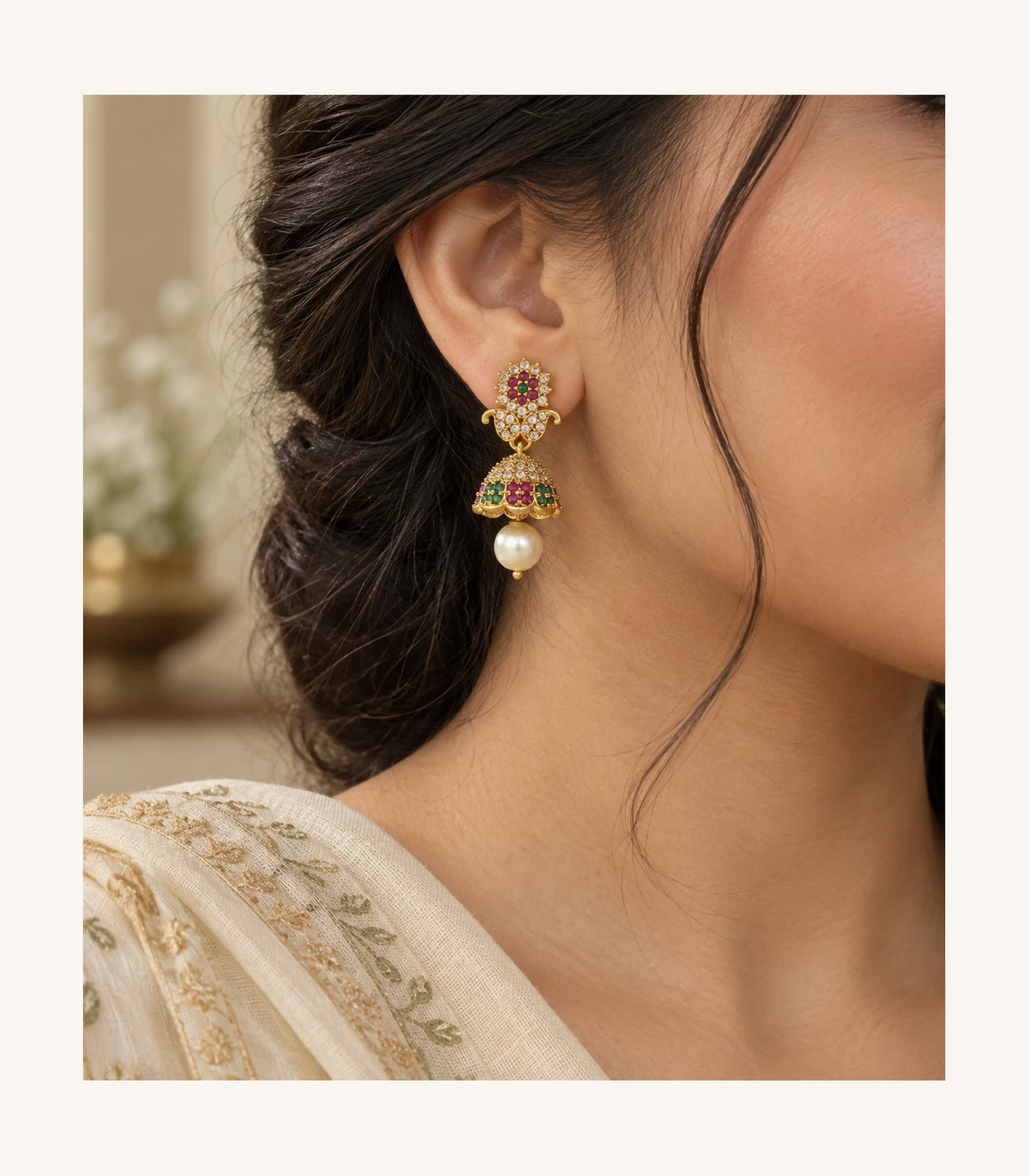 Editorial side view of one gold-tone magenta and green earring worn with a cream outfit