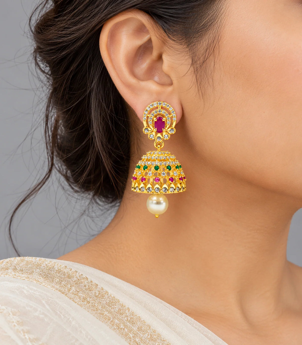 Gold-tone magenta and green jhumka earrings with cream pearl-like drops worn with an ivory sari