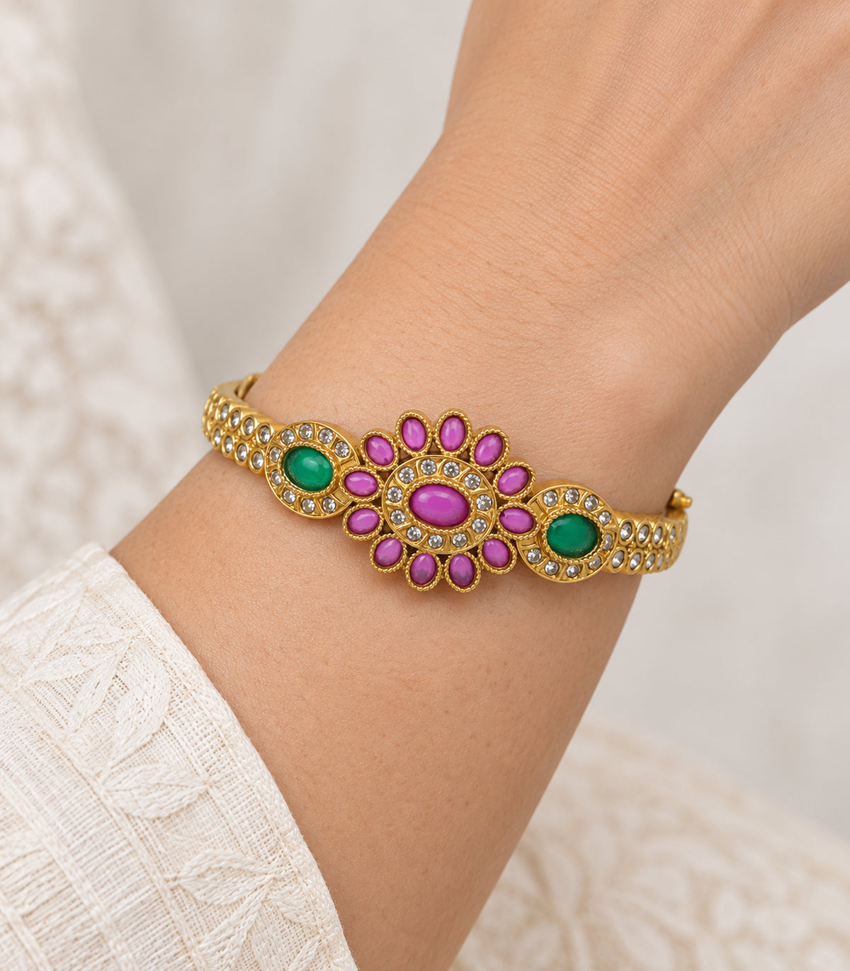 Closeup of the magenta oval flower and green halo details on the worn gold-tone bangle