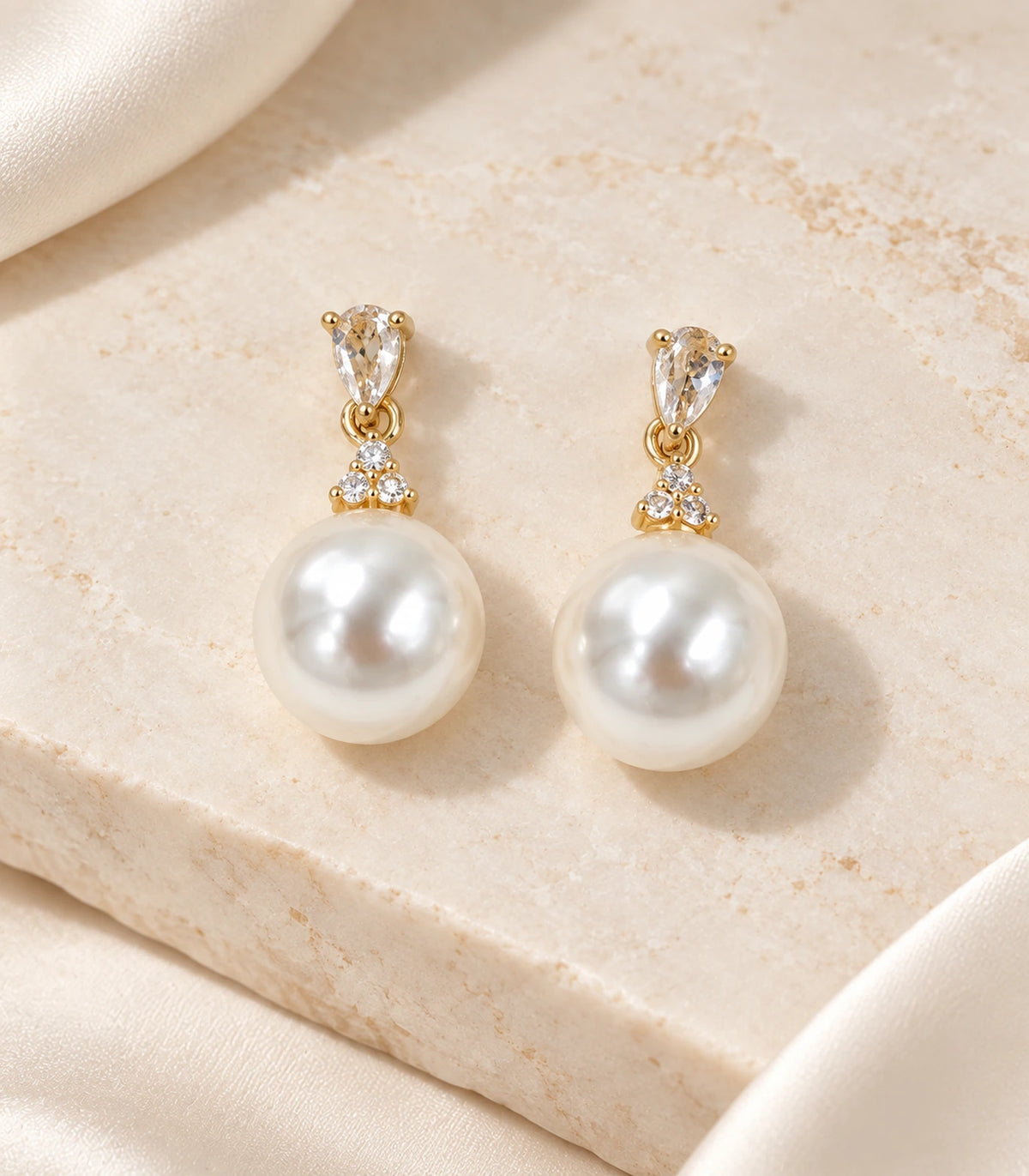 Matching pair of gold-tone crystal-style and white pearl-style drop earrings arranged on a pale stone surface.