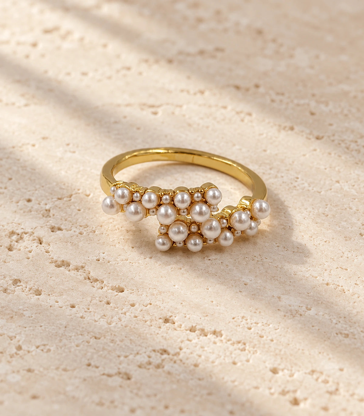 Gold Pearl Cluster Crossover Ring on a textured stone surface