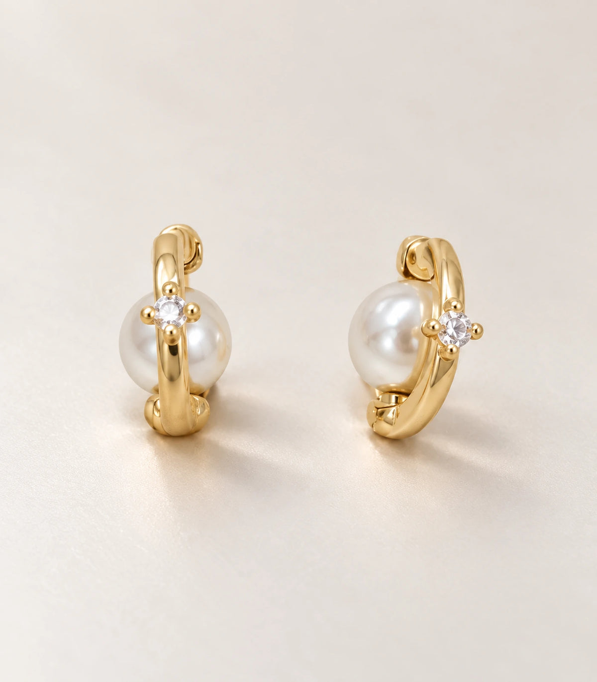 Close view of the matching gold-tone orbit huggie earring pair on pale fabric