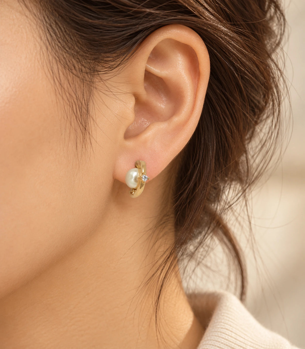 Gold-tone orbit huggie earring with pearl-style accent and clear stone in a second worn composition