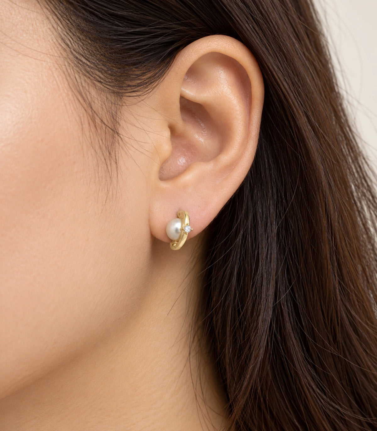 Gold-tone orbit huggie earring with pearl-style accent and clear stone worn on one ear
