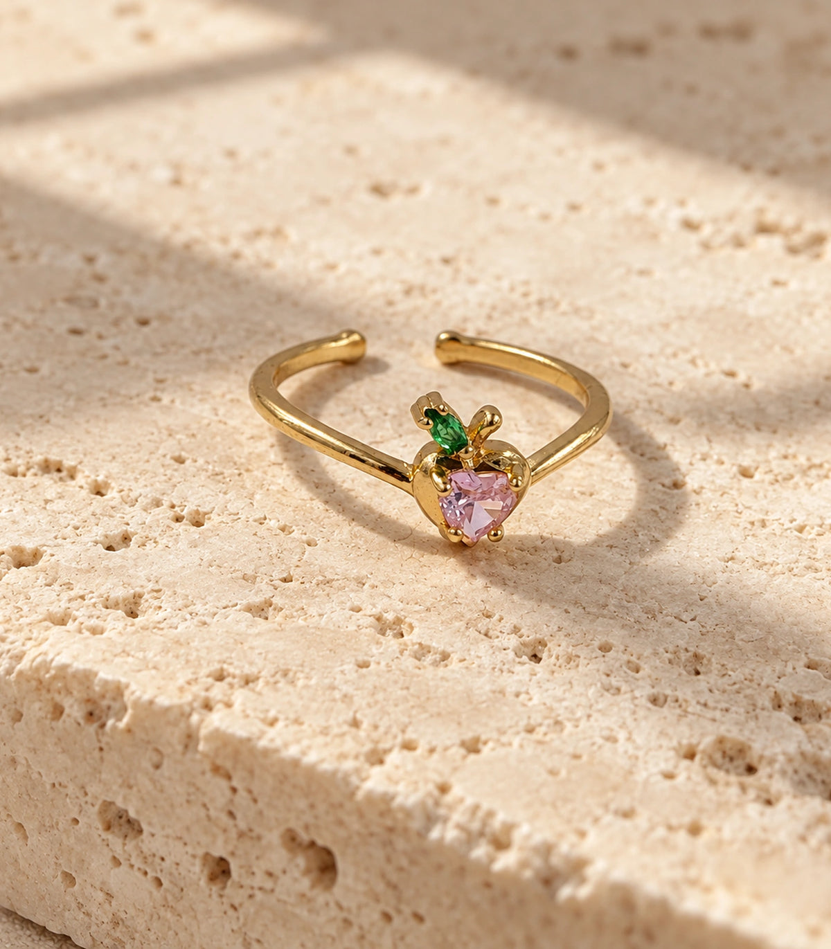 Complete gold pink heart and green leaf open ring on a neutral stone surface