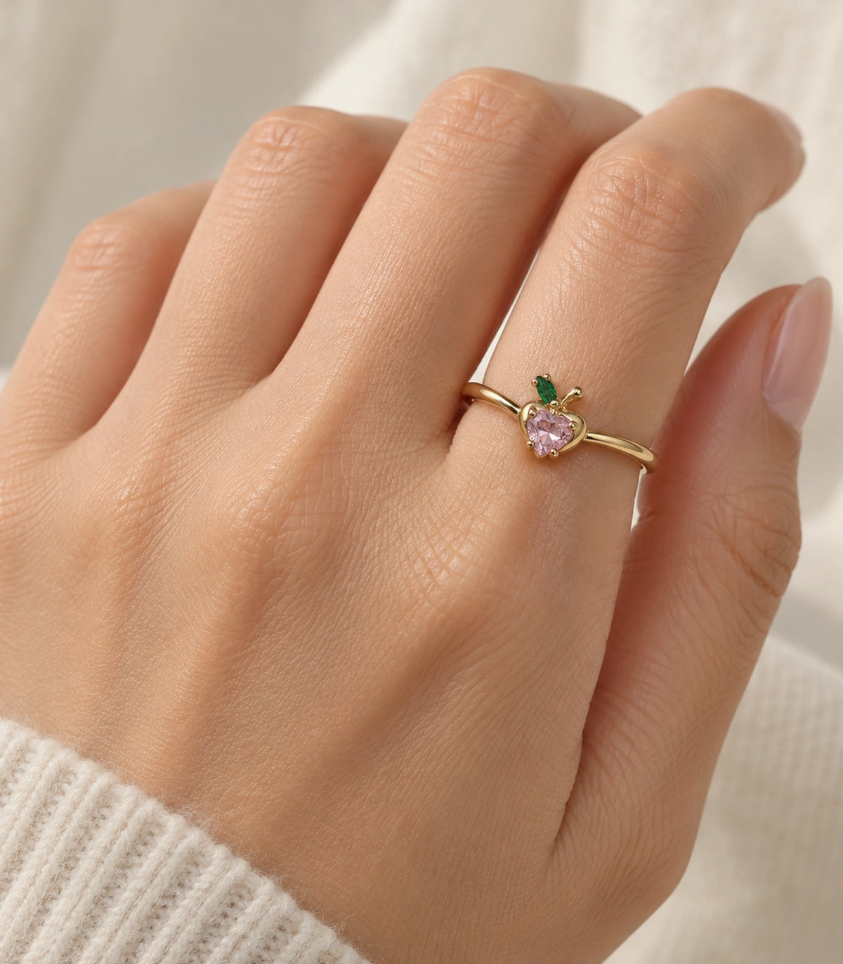 Gold pink heart and green leaf ring worn on a hand with a cream knit sleeve