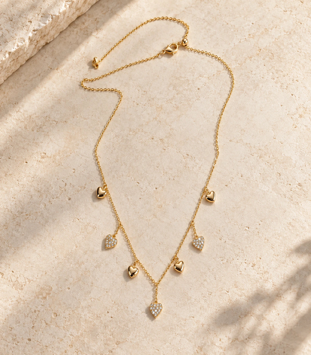 JIMIKI Gold Seven Heart Charm Necklace - complete seven-heart necklace in a styled flat lay #color_gold