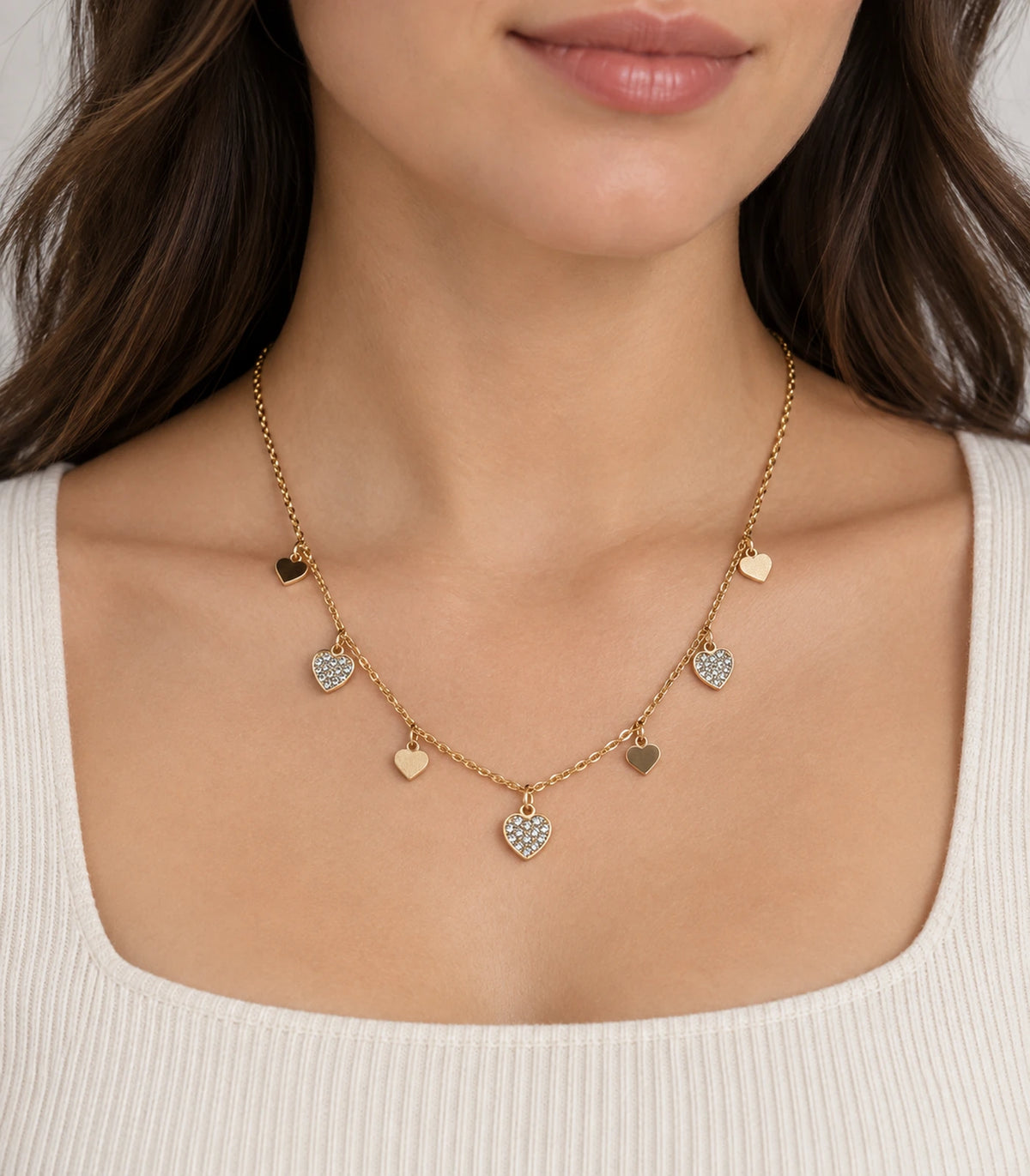 JIMIKI adjustable gold-tone seven heart charm necklace, seven-heart necklace worn with a cream knitted top #color_gold