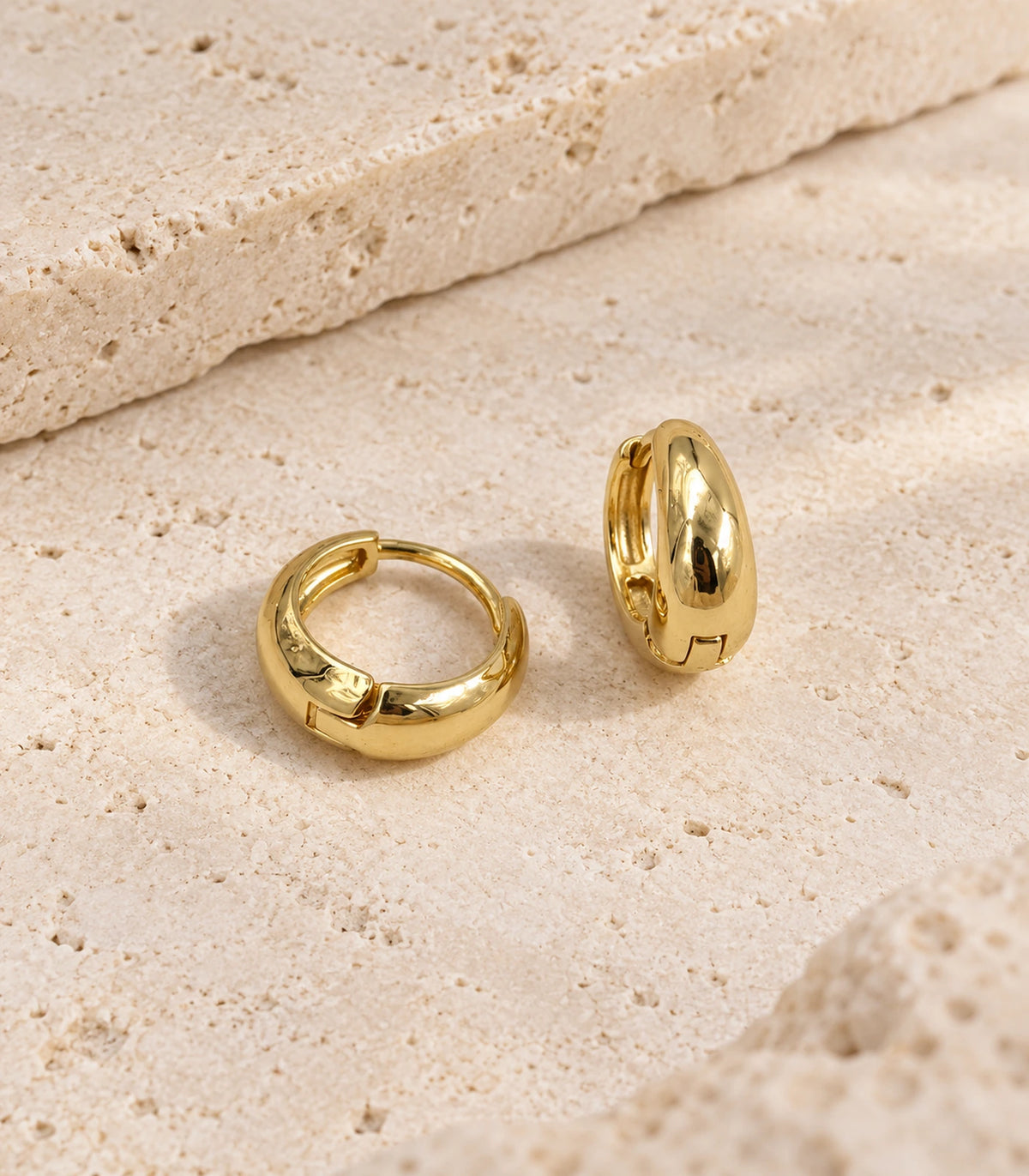 JIMIKI Smooth Tapered Huggie Earrings in Gold Tone — editorial flat lay #color_gold-tone