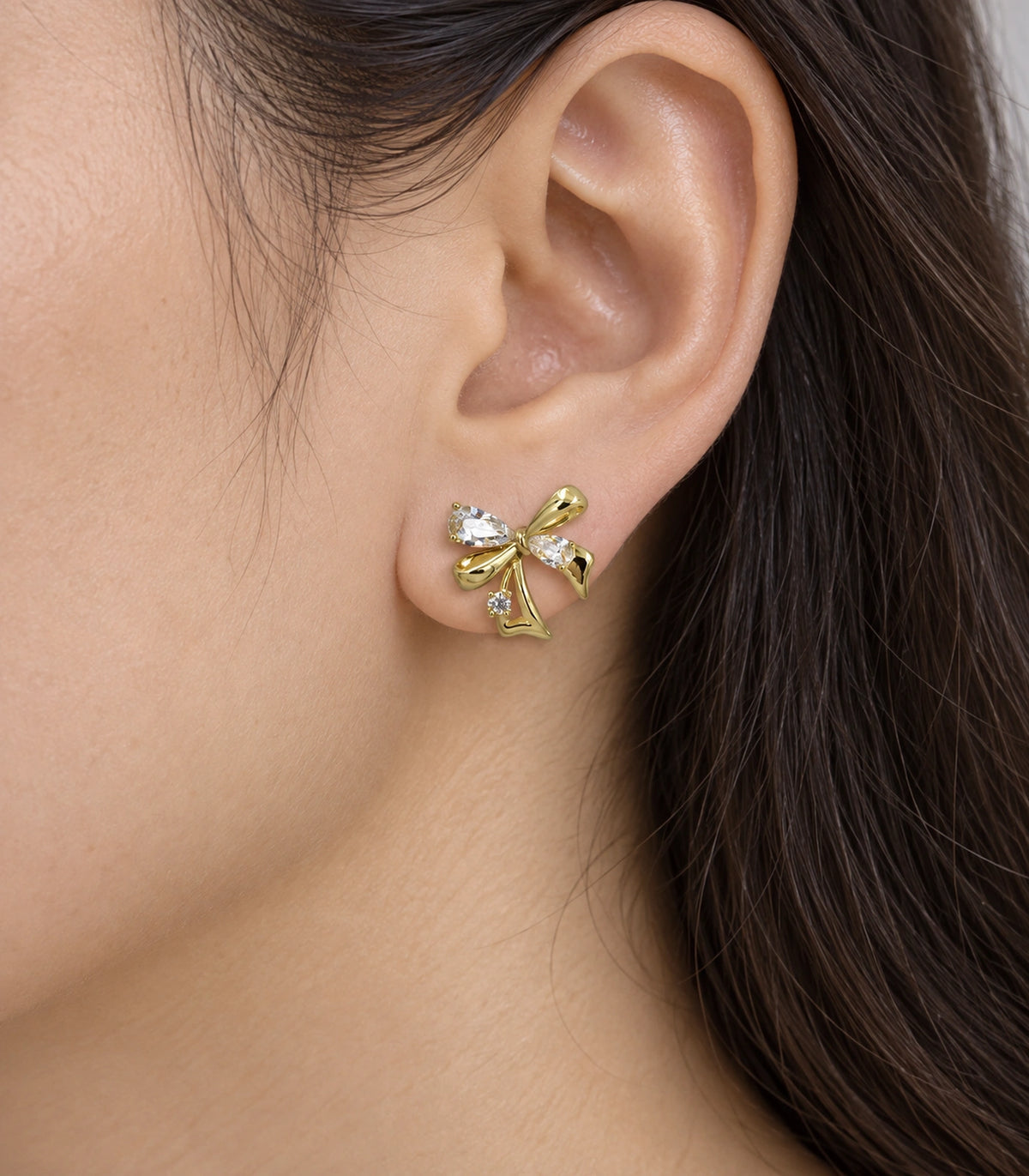 JIMIKI Asymmetric Crystal Bow Stud Earring Pair in Gold / Clear, close-up detail #color_gold / clear