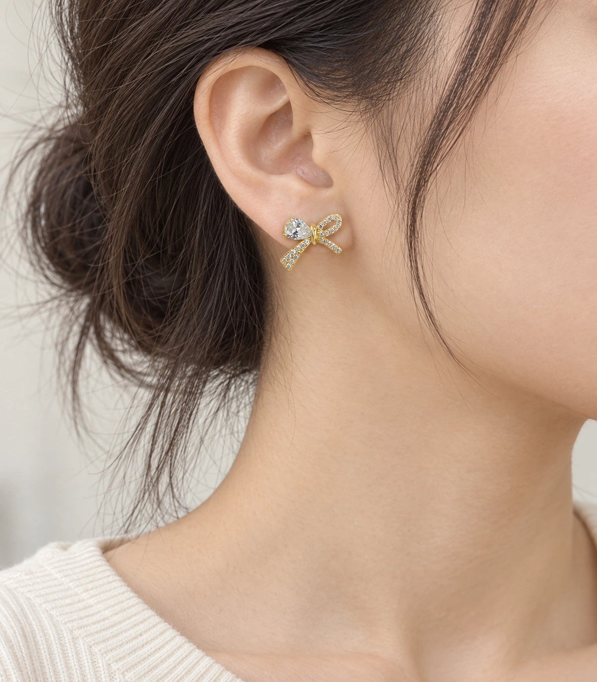 JIMIKI Gold-Tone Asymmetric Crystal Bow Stud Earrings in Gold / Clear, model wearing view