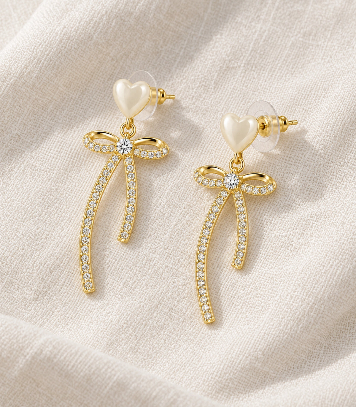 JIMIKI Heart Crystal Ribbon Bow Drop Earring Pair in Gold-tone / Cream, editorial flat lay #color_gold-tone / cream