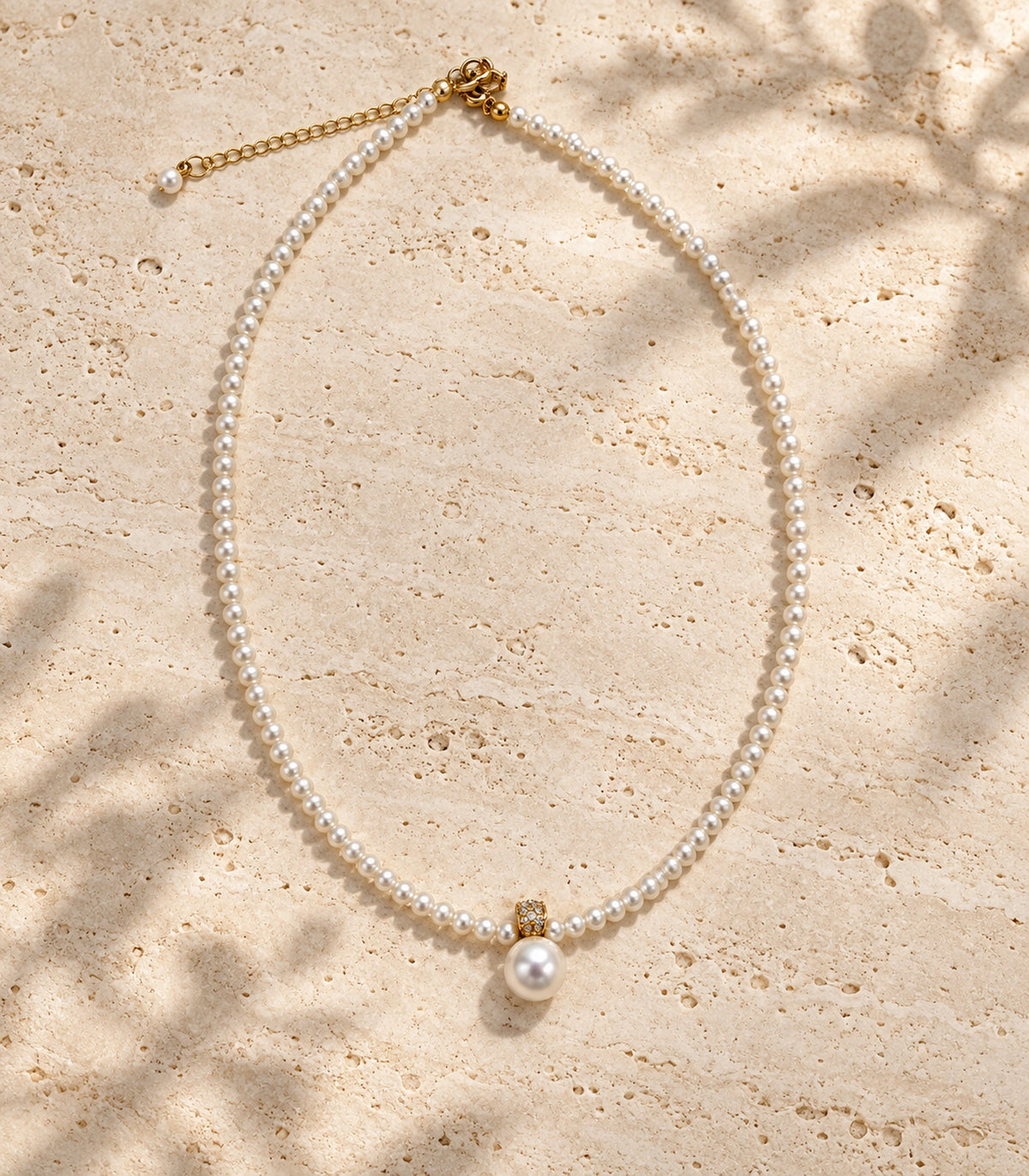 JIMIKI Gold-Tone Crystal Bail Pearl Drop Necklace in Gold-tone / white, arranged in an editorial flat lay