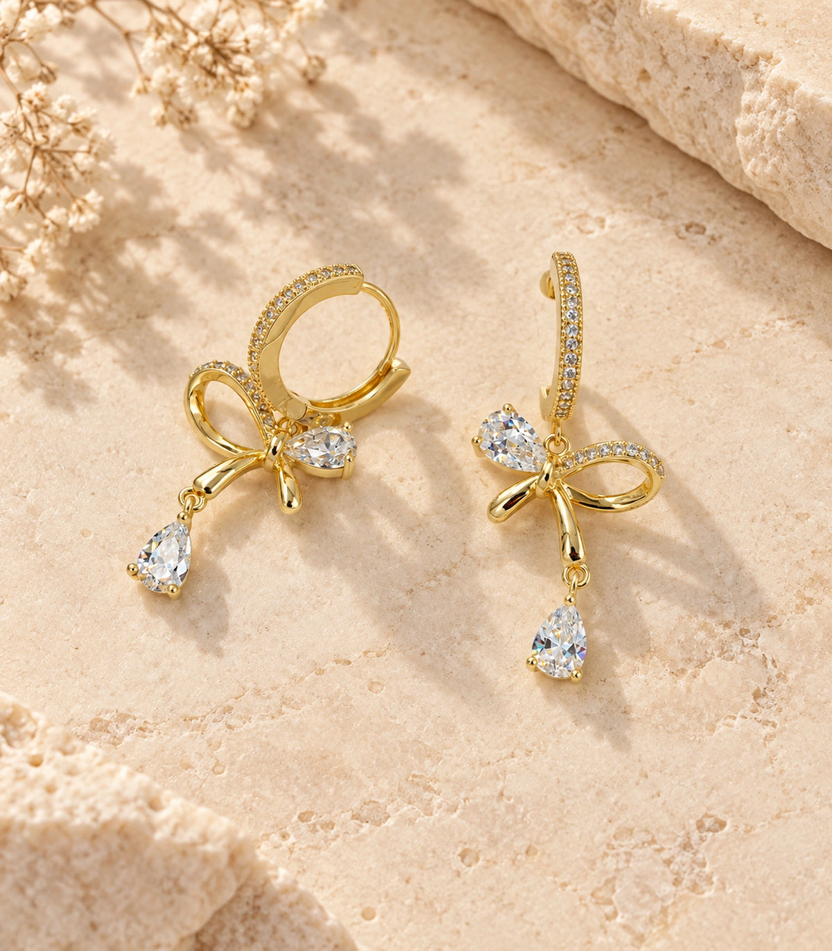 JIMIKI Gold-Tone Crystal Bow Drop Huggie Earrings in Gold / Clear, editorial flat lay