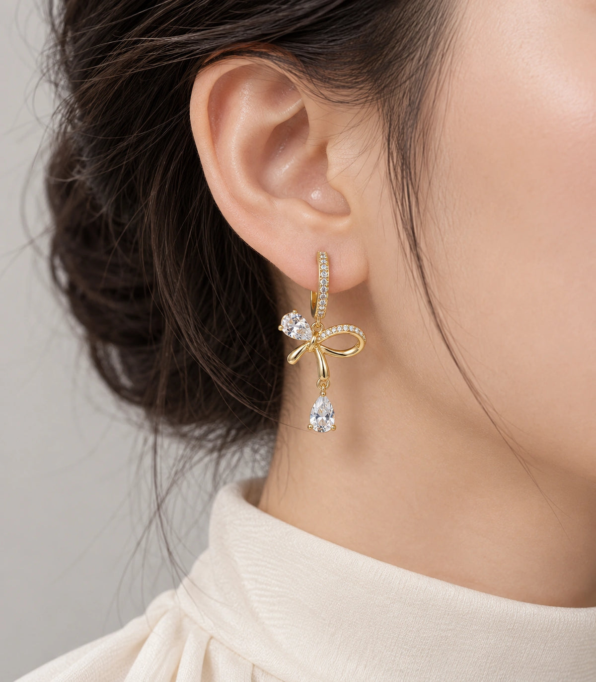 JIMIKI Gold-Tone Crystal Bow Drop Huggie Earrings in Gold / Clear, model wearing view