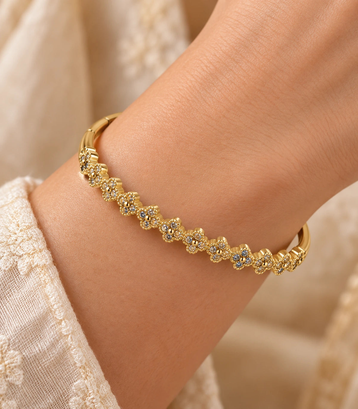JIMIKI Gold-Tone Crystal Clover Row Bangle — close-up of the bangle worn on the wrist #color_gold-tone / clear